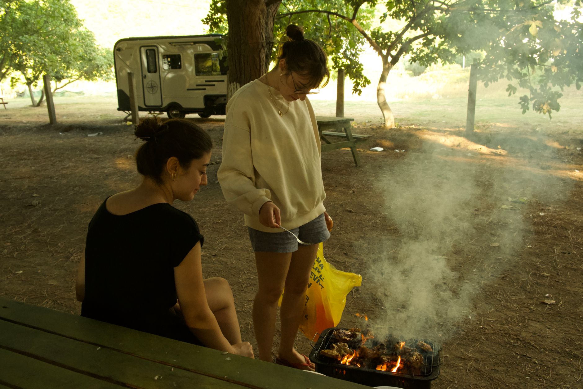 Two people grilling at a campsite near a camper