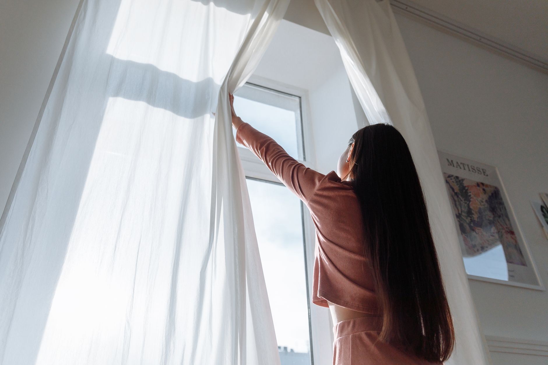 A woman opening sheer curtains