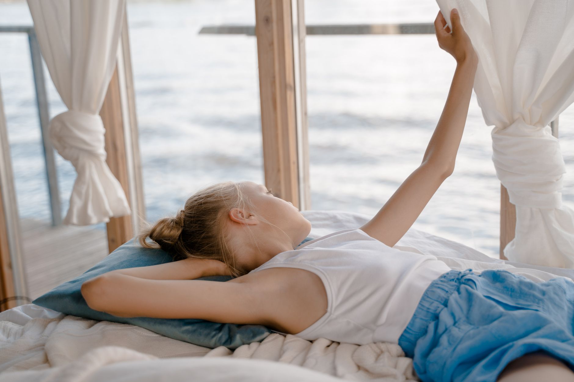 A woman stretching on a bed by a window