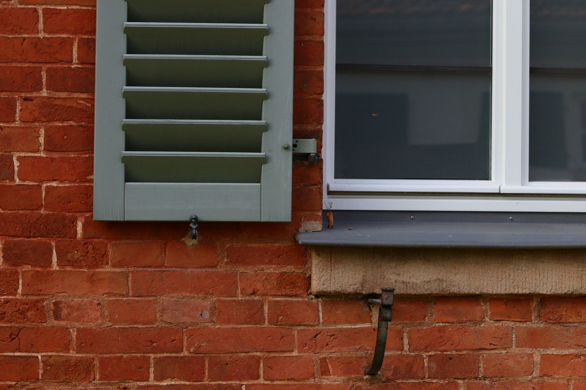 A window with a gray shutter on a red brick wall