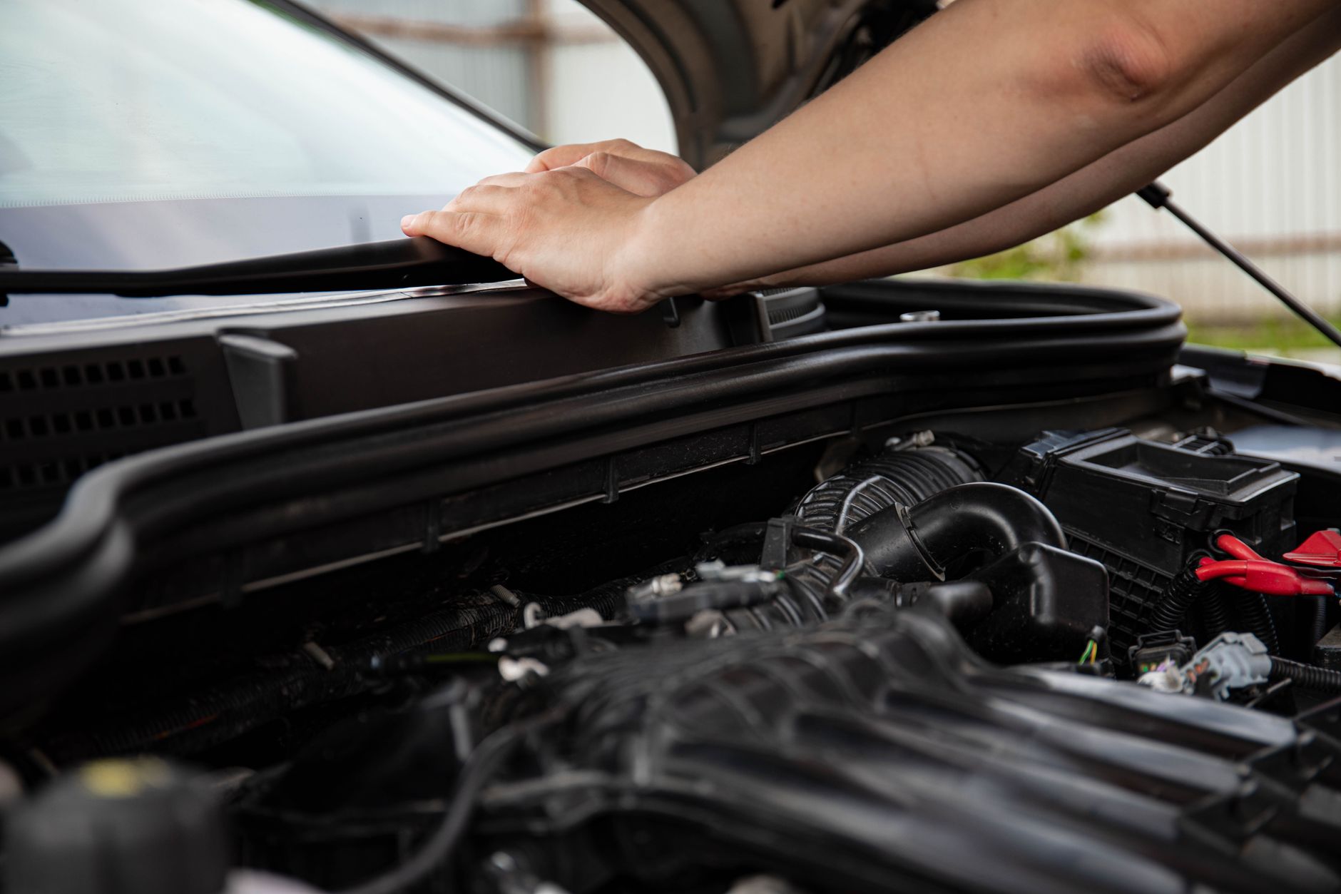 A hand propping open a car hood over the engine