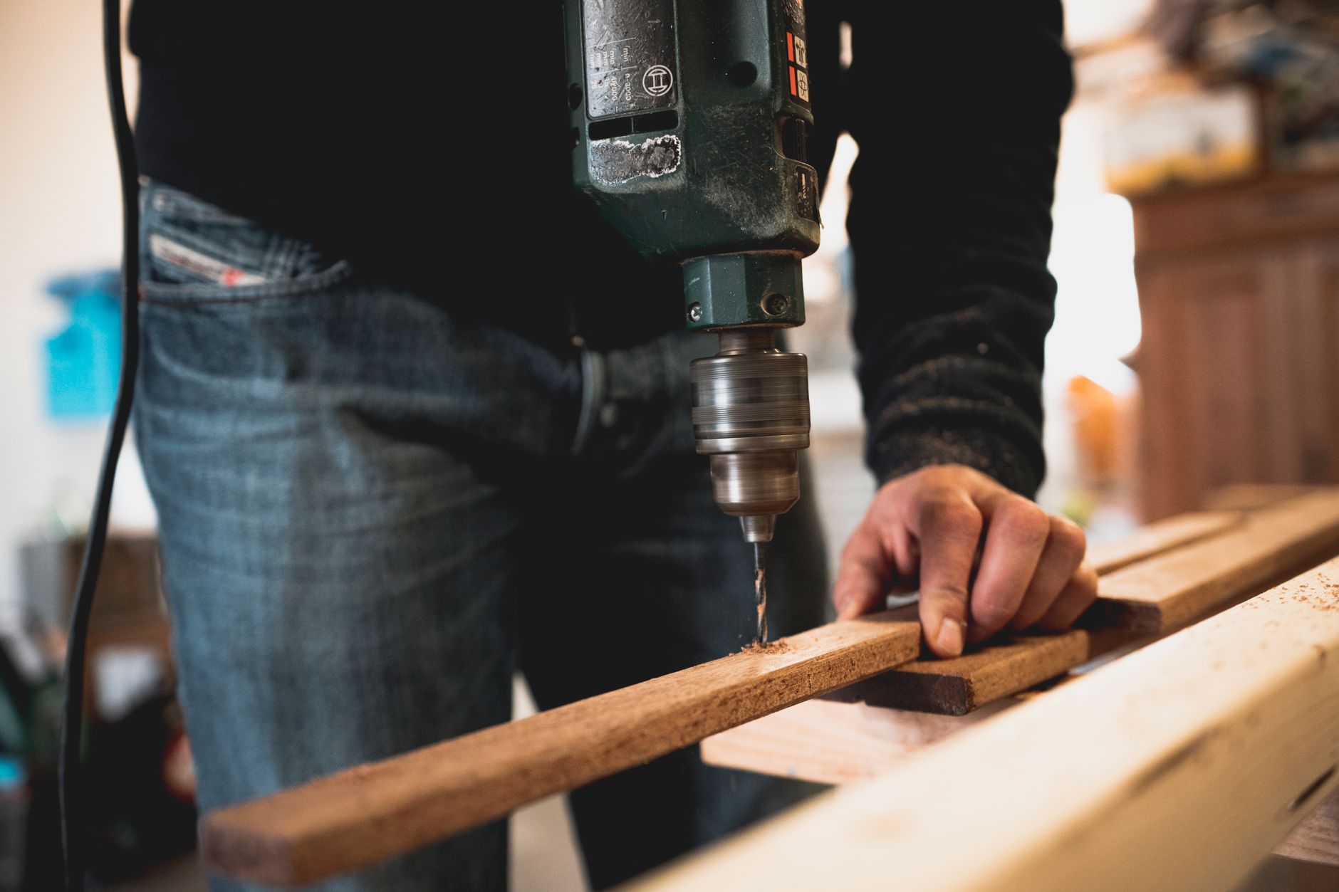 A person drilling a board on a work table